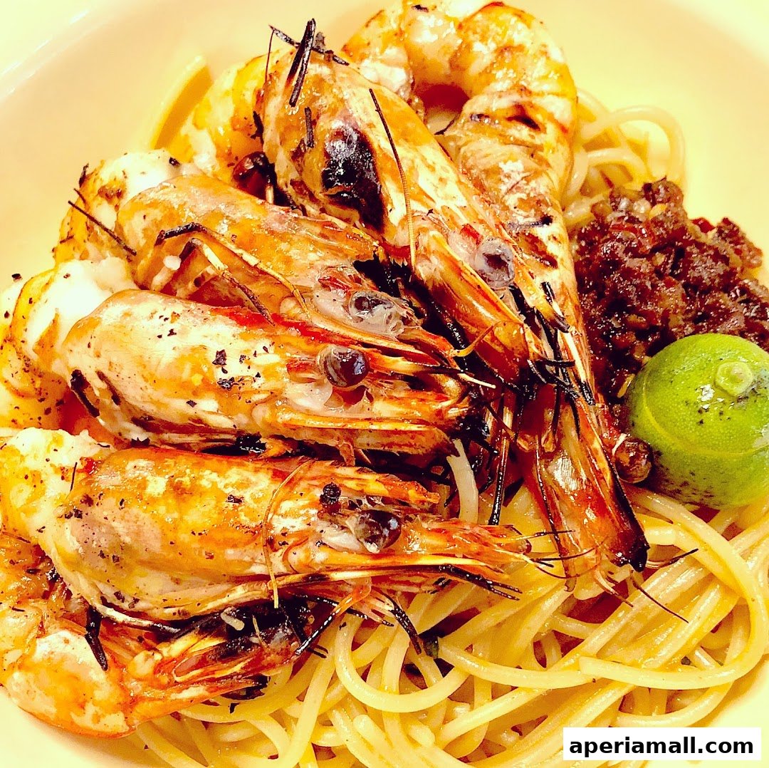 A close-up shot of spaghetti topped with grilled prawns, a lime wedge, and a side of relish.