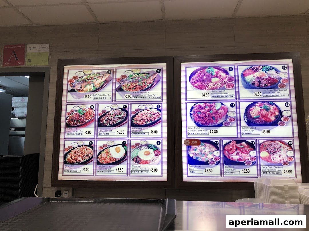 A brightly lit menu board displaying various Korean food dishes with prices.