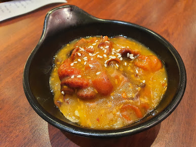 A black bowl filled with food in orange sauce, topped with sesame seeds.