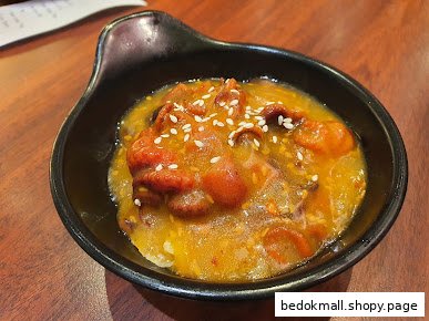 A black bowl filled with food in orange sauce, topped with sesame seeds.