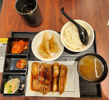 A meal set with chicken, rice, gyoza, and side dishes on a wooden table.