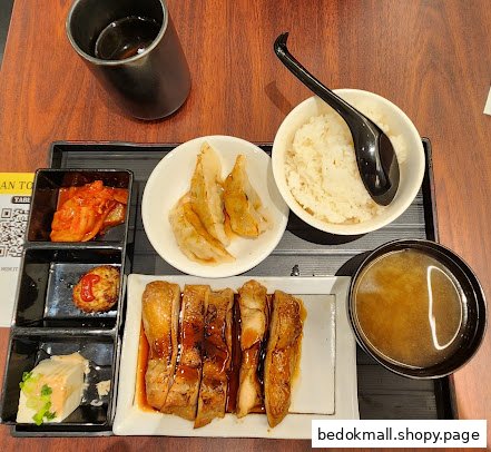 A meal set with chicken, rice, gyoza, and side dishes on a wooden table.