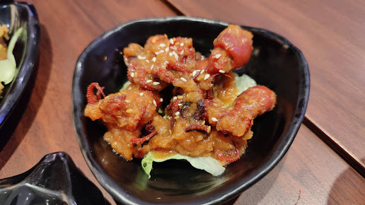 A black bowl of fried baby octopus with sauce and sesame seeds.