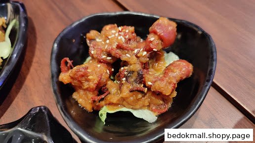 A black bowl of fried baby octopus with sauce and sesame seeds.