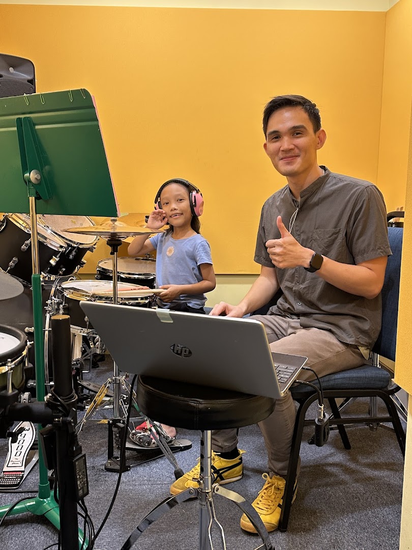 Adult and child in a music room with drums and a laptop.