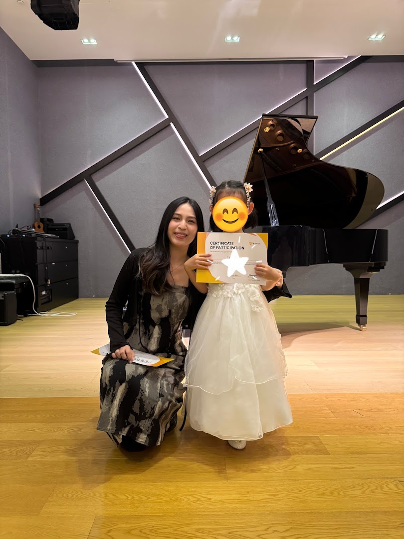 Adult and child with certificate in a music room with a grand piano.