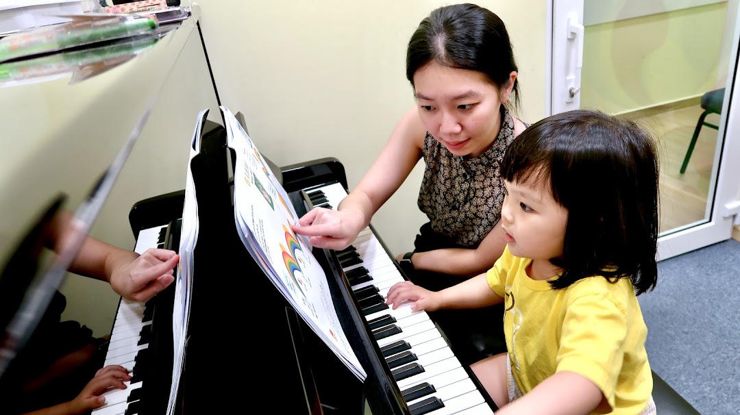 An adult teaches a child to play piano during a music lesson.