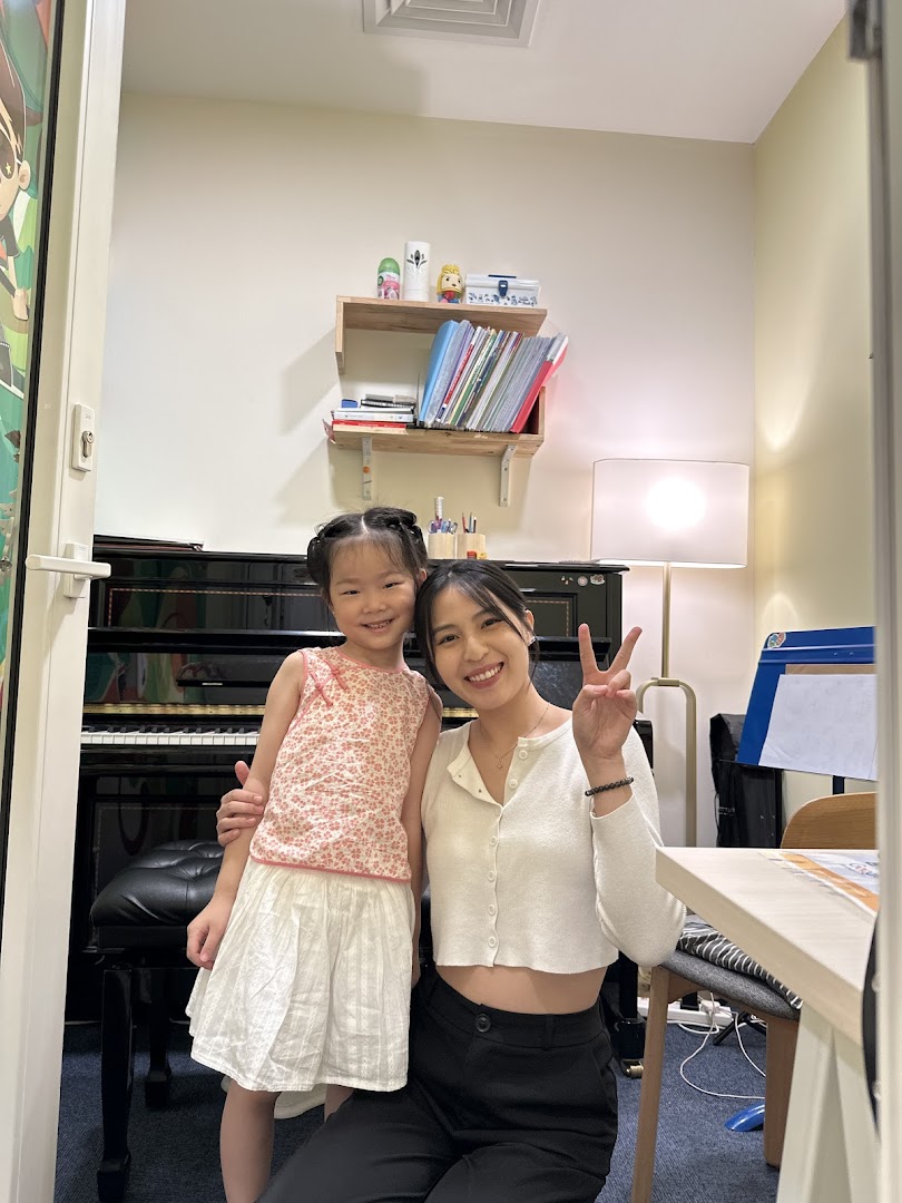 An adult and child pose in a music academy room with a piano.