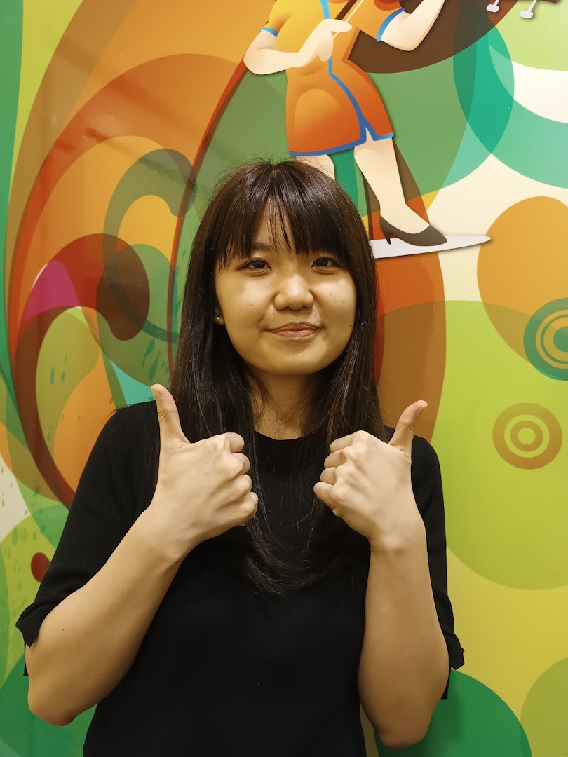Smiling person gives thumbs up against a colorful wall.