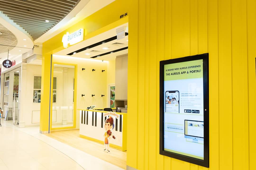 Bright yellow music academy shop front with reception desk and digital display.