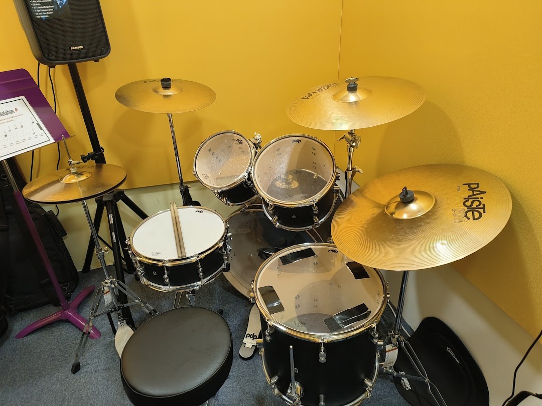 A black drum set with cymbals and a music stand in a yellow room.