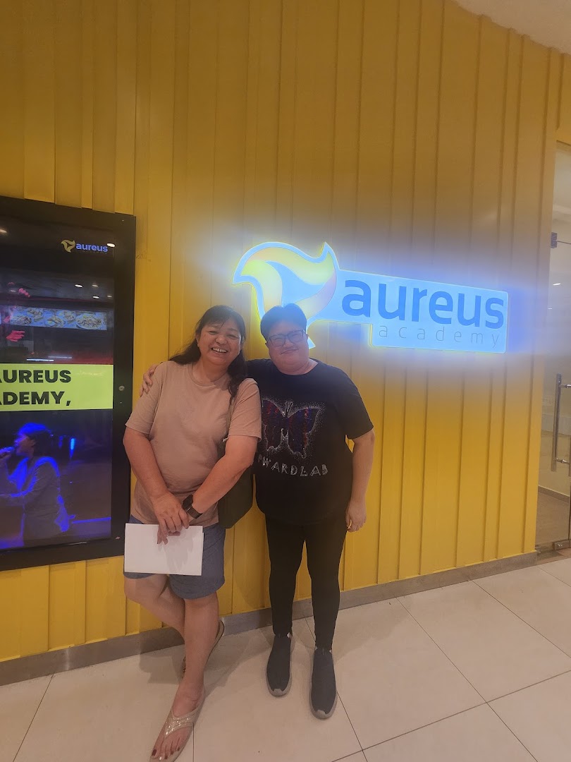 Two people stand in front of the Aureus Academy shop entrance with its glowing sign.