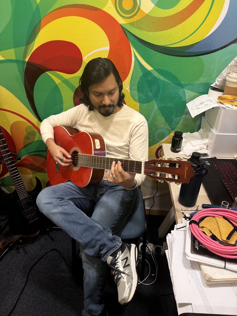 A person plays a red acoustic guitar in a colorful room.