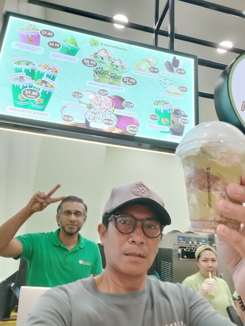 A person holds a drink in front of a large digital menu board.