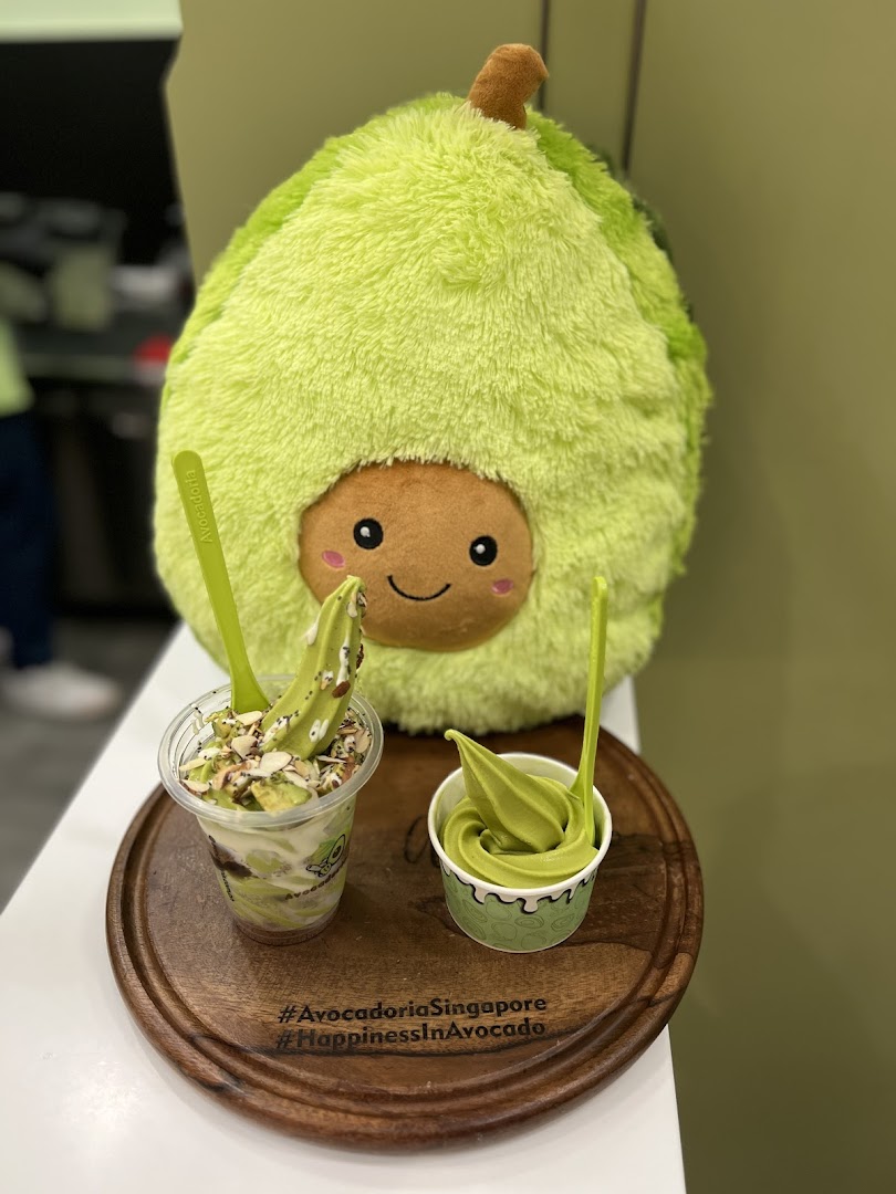 Two avocado desserts and a large avocado plush toy on a wooden tray.
