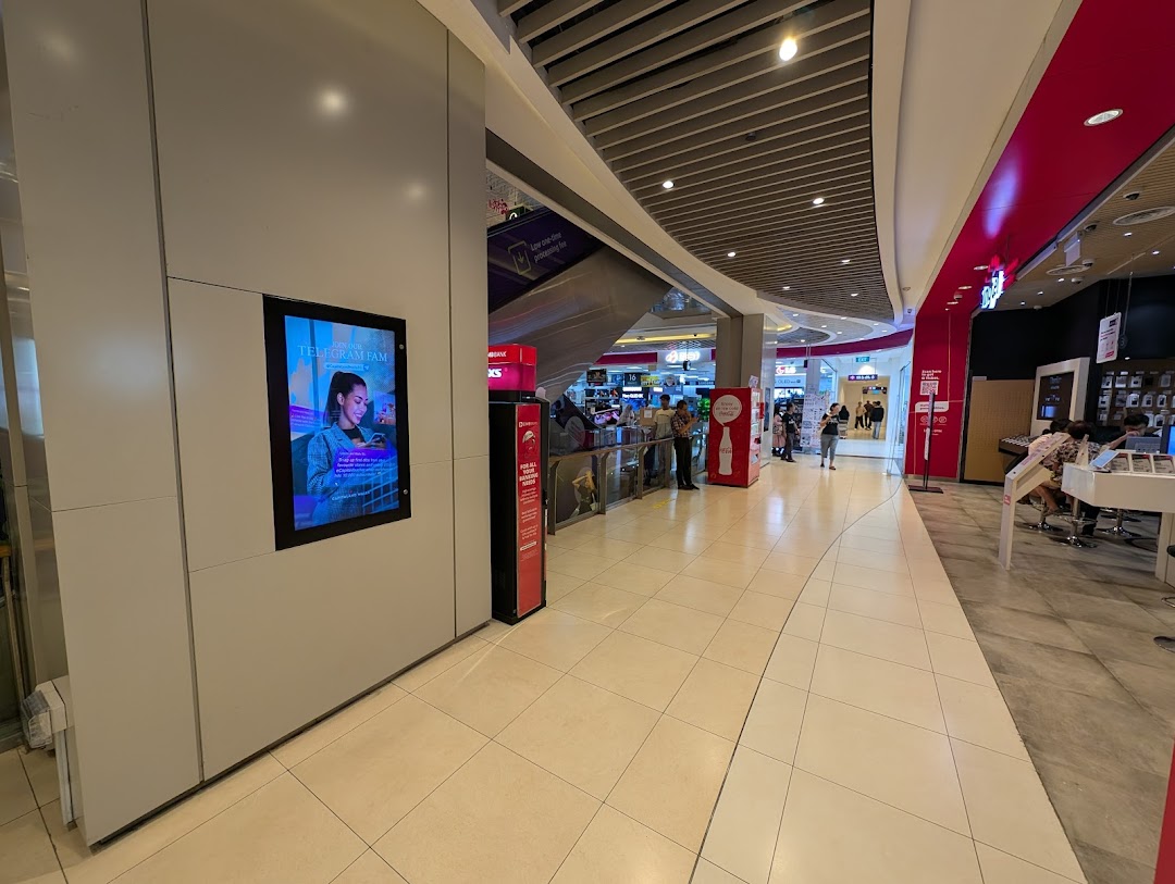 Mall corridor with a shop entrance, people, and a digital display.