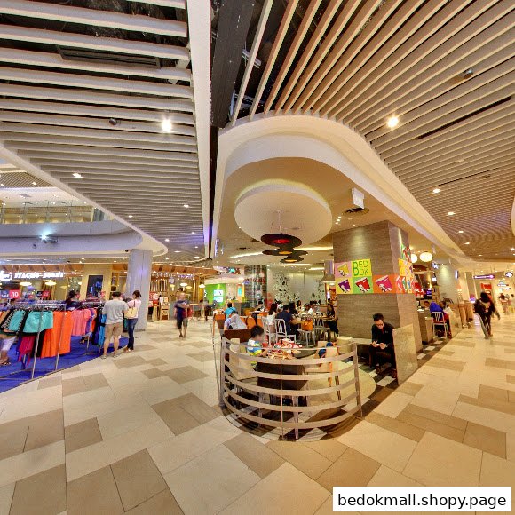 Interior view of a busy shopping mall with various shops and a food court area.