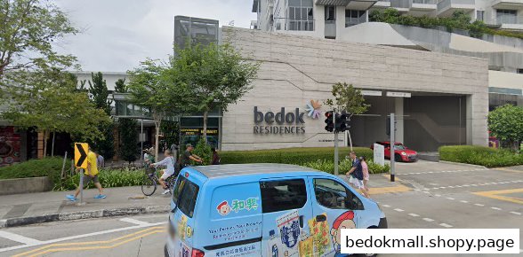 Street view of a large building complex with people, trees, and a blue van.