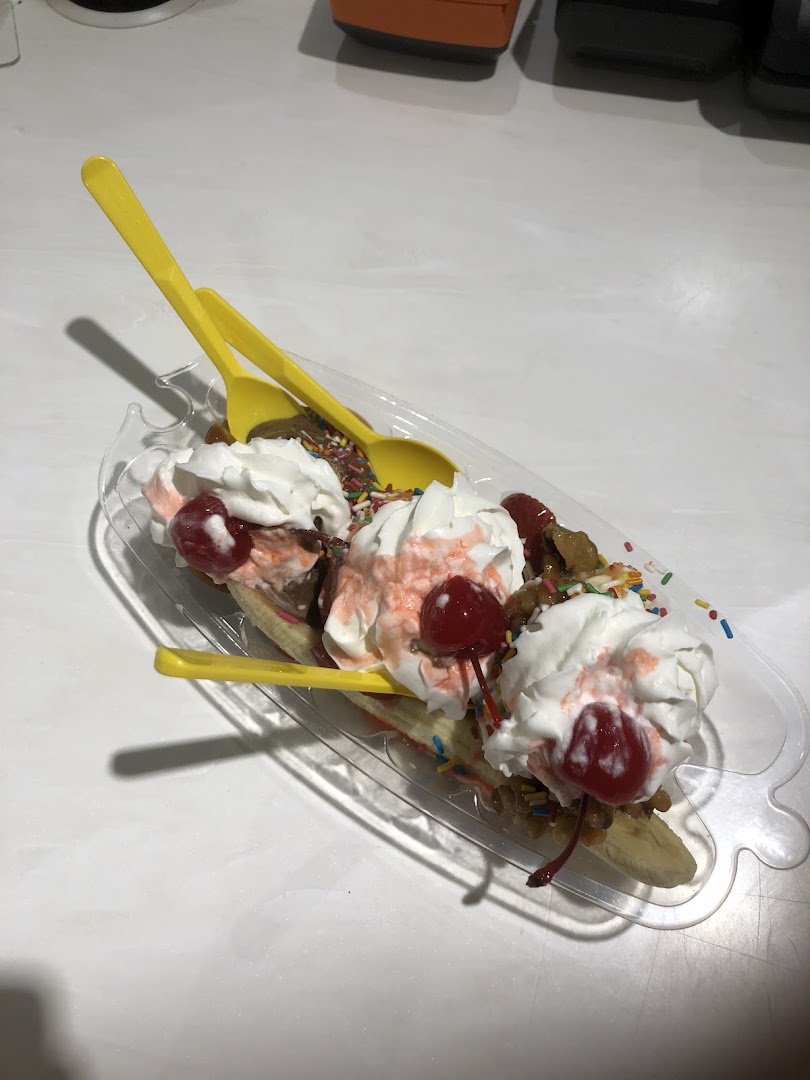 A banana split dessert with whipped cream, cherries, and sprinkles in a clear dish.