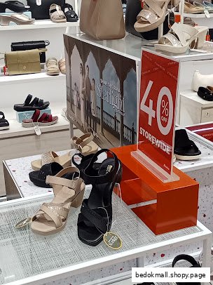 Interior view of a shoe store displaying shoes, handbags, and a sale sign.