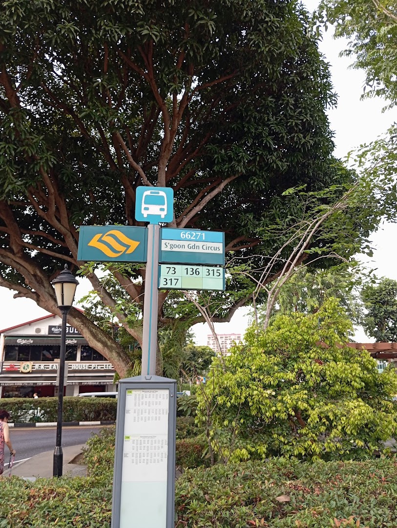 Outdoor scene showing a bus stop sign and route information near a large tree.