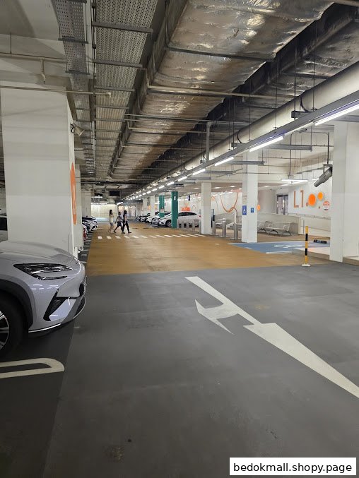 View of a brightly lit indoor mall carpark with cars and pedestrians.