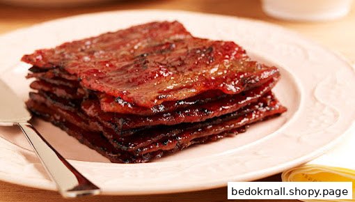 Stack of glossy, reddish-brown meat slices on a plate with a serving utensil.