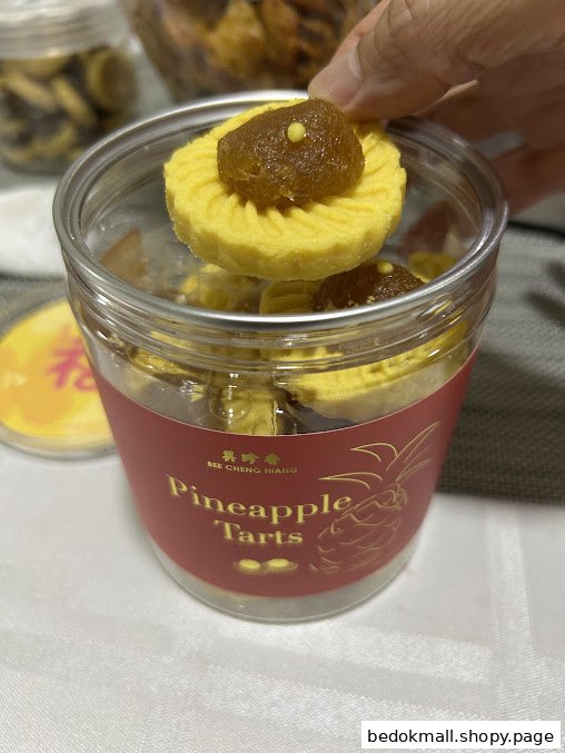 A hand holds a pineapple tart over a container labeled 'Pineapple Tarts'.