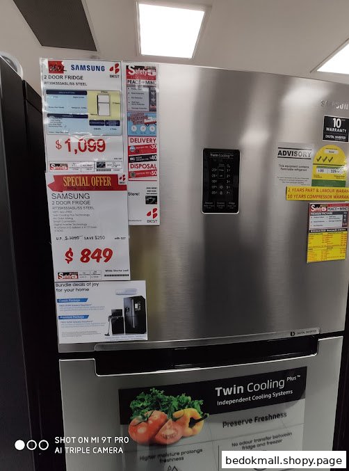 A silver Samsung refrigerator with price tags and product information in a store.