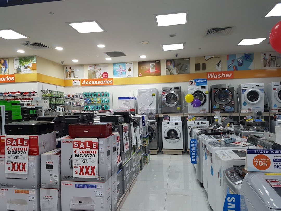 Interior view of an electronics store displaying printers, accessories, and washing machines.
