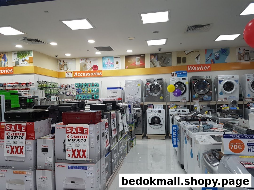 Interior view of an electronics store displaying printers, accessories, and washing machines.