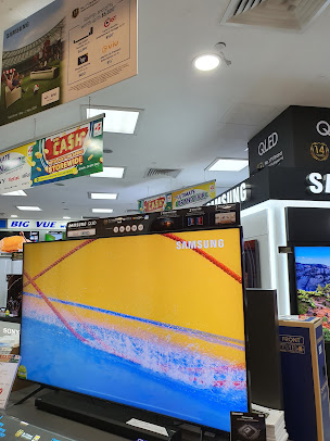 Interior view of an electronics store with large TVs and promotional banners.