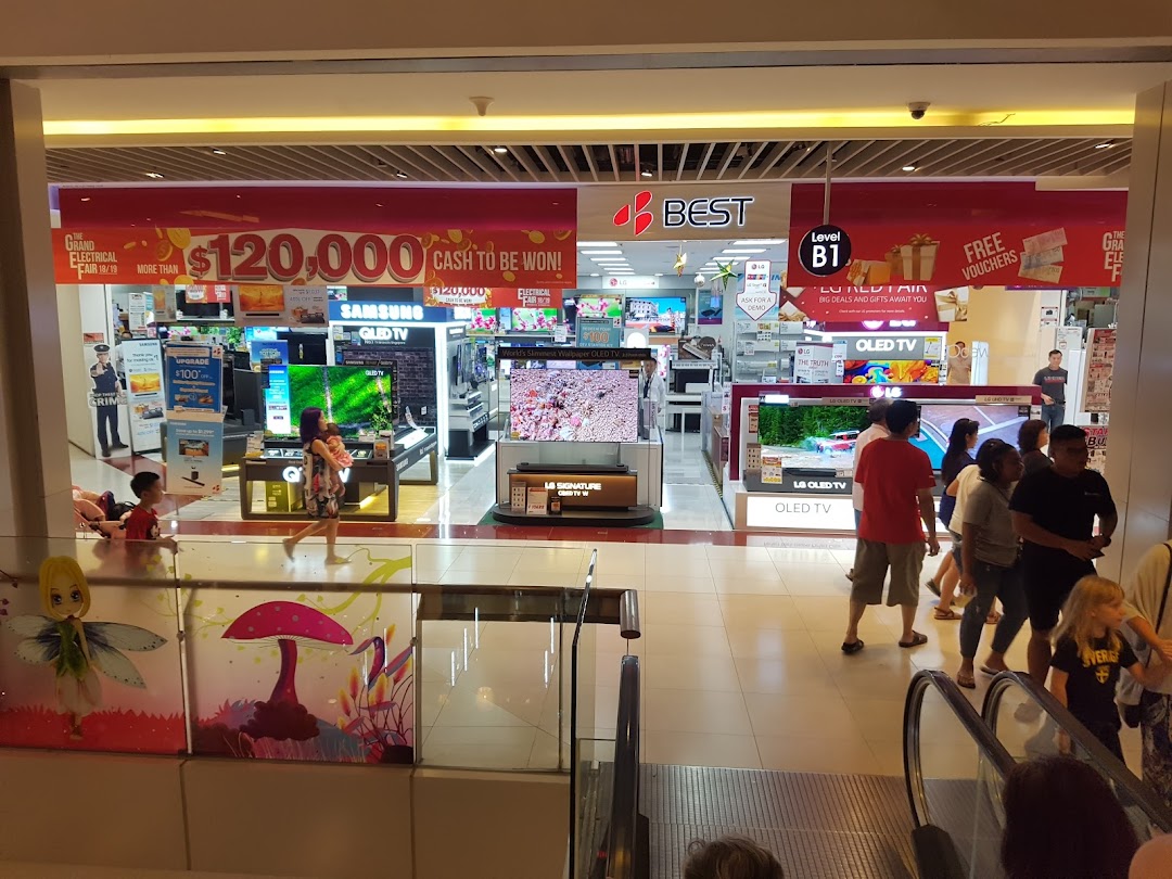 Entrance of an electronics store with TVs on display and people walking by.