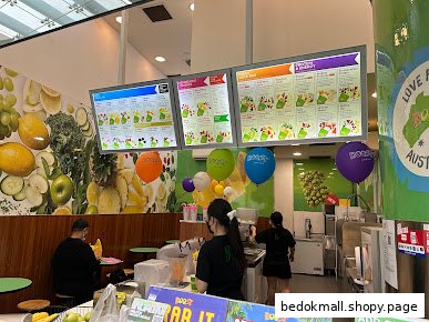 Interior of a Boost Juice shop with staff, a customer, and digital menu boards.