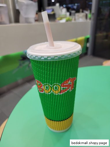A green Boost Juice cup with a straw sits on a light green table.