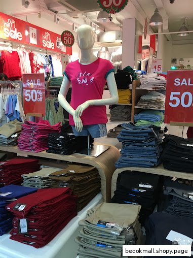 Mannequin and folded clothes on display in a clothing store with sale signs.