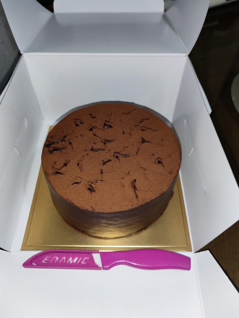 A chocolate cake in a white box with a pink plastic knife.