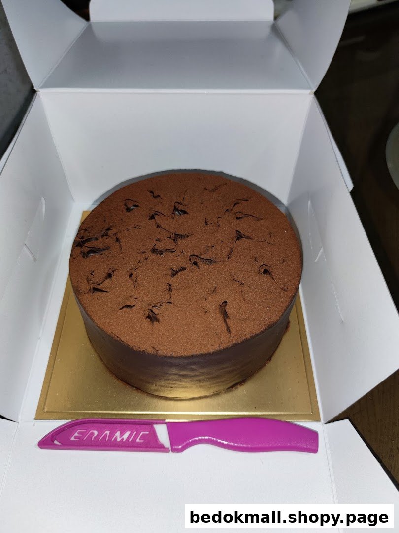 A chocolate cake in a white box with a pink plastic knife.