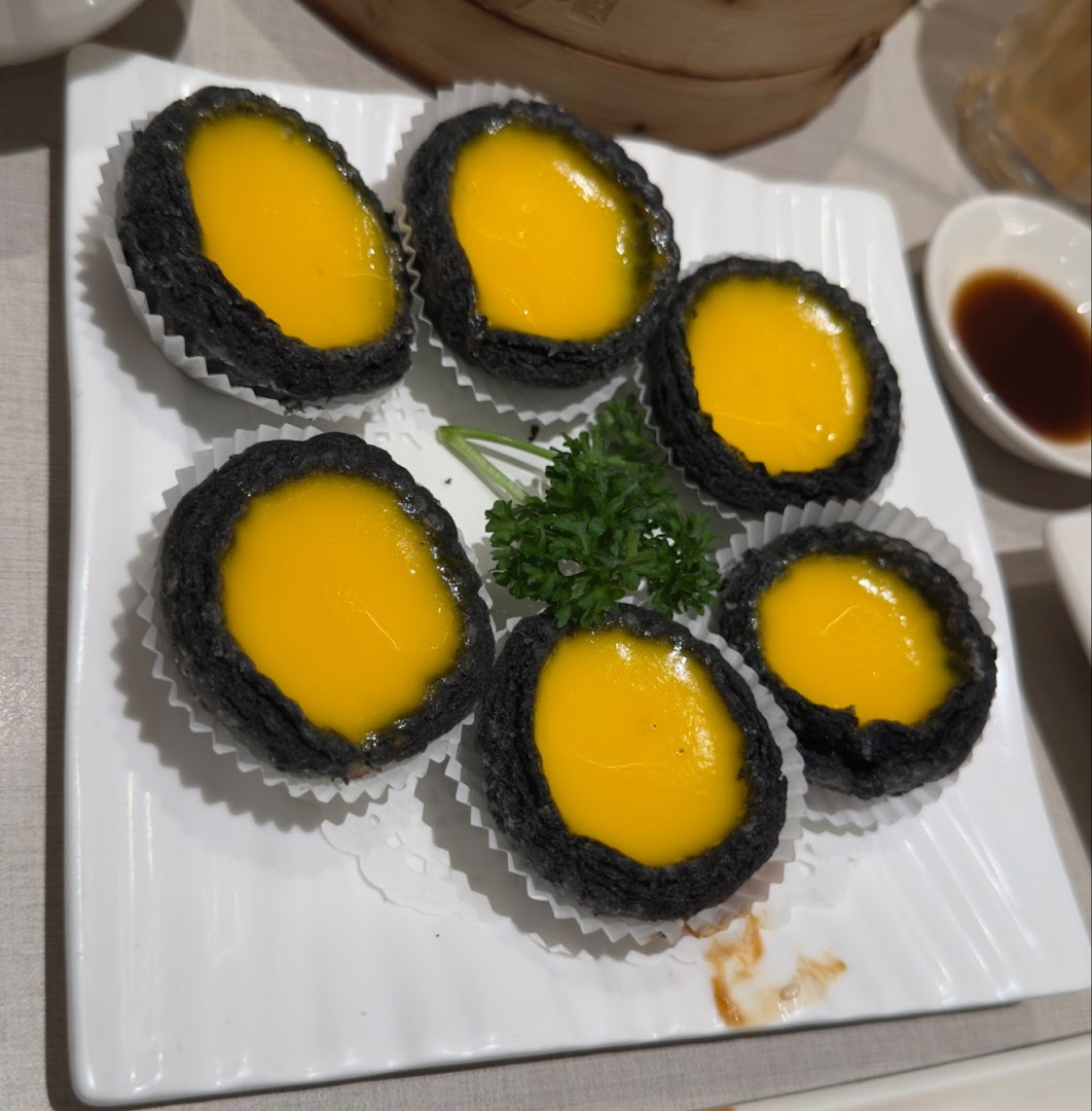 Six black-crusted tarts with yellow filling on a white plate.