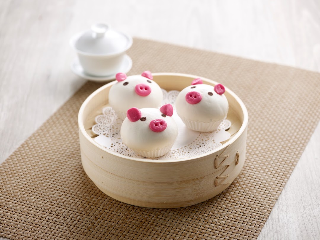 Three pig-shaped buns in a bamboo steamer with a teacup in the background.