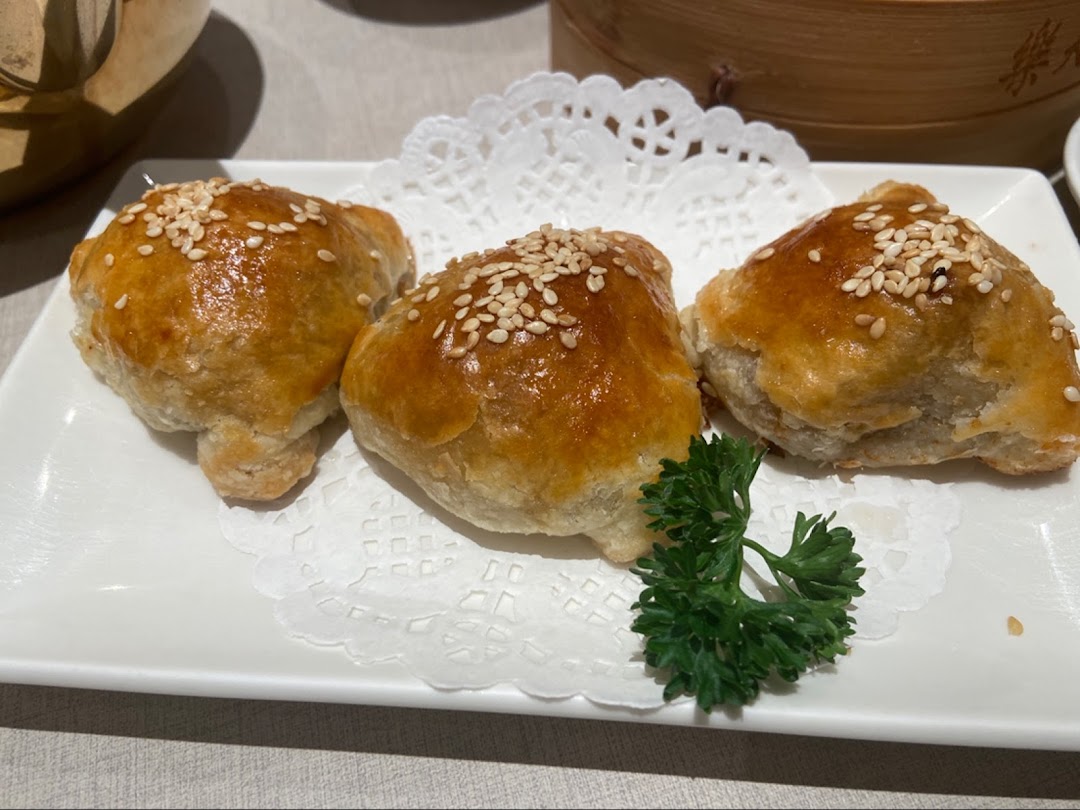 Three golden baked pastries with sesame seeds on a white plate.