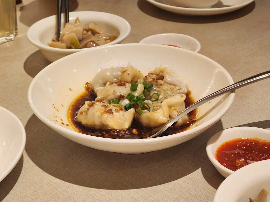 A bowl of dumplings with sauce and other dishes on a table.