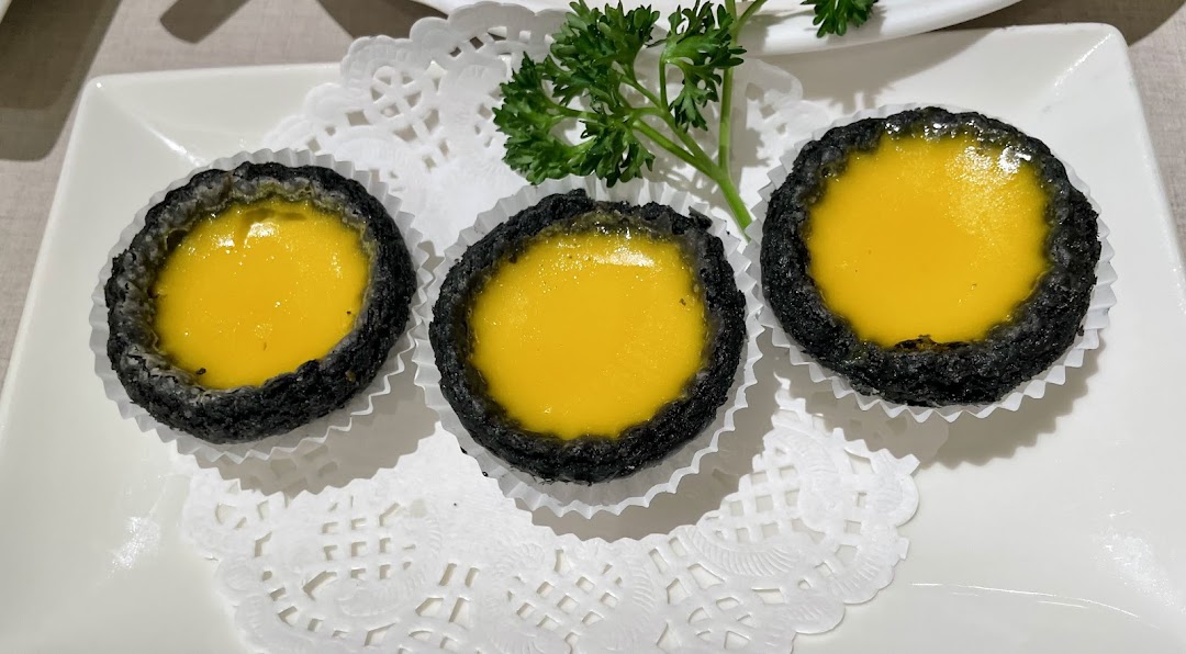 Three black-crusted egg tarts with yellow filling on a white plate.