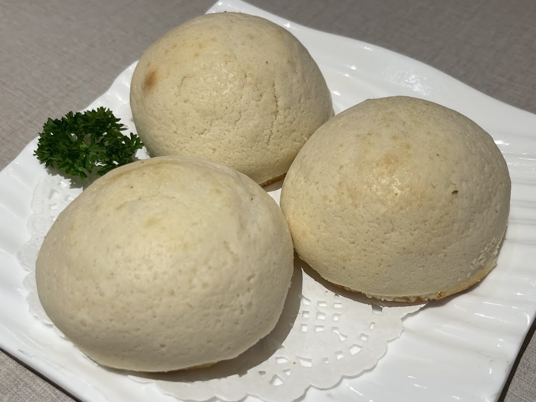 Three light-colored buns on a white plate with a green garnish.