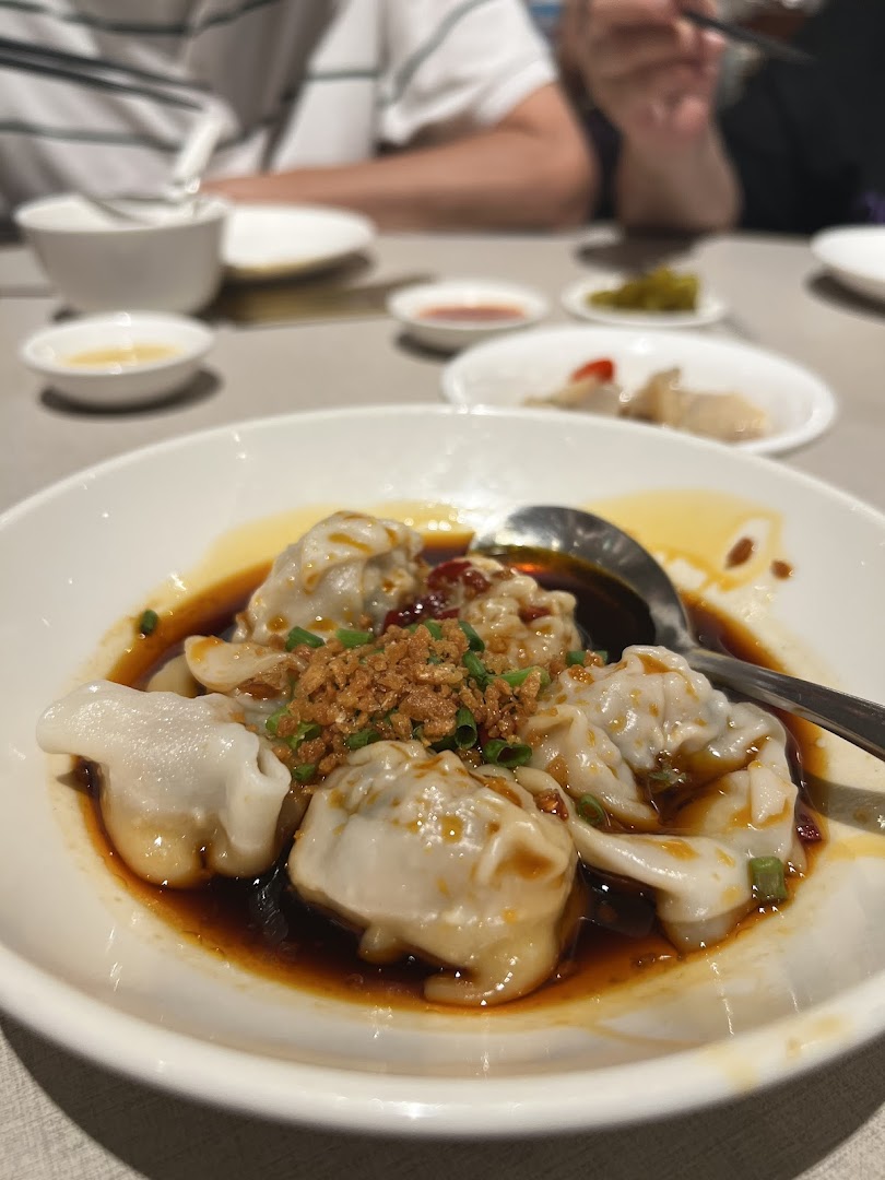 A close-up of a plate of dumplings in sauce with crispy toppings on a table.