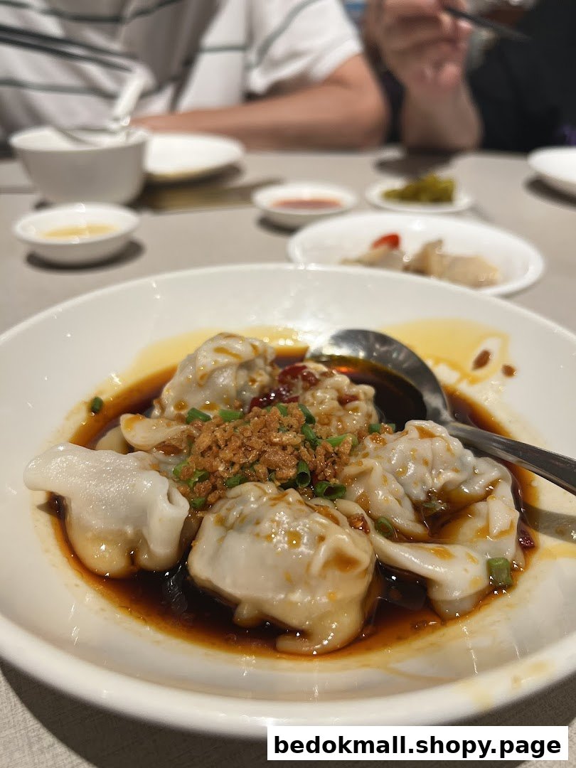 A close-up of a plate of dumplings in sauce with crispy toppings on a table.