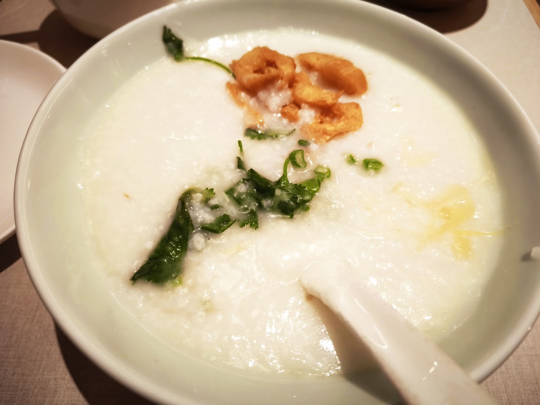Close-up of a bowl of congee with fried dough and greens.