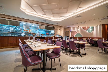 Restaurant interior with dining tables, purple chairs, and a visible kitchen area.