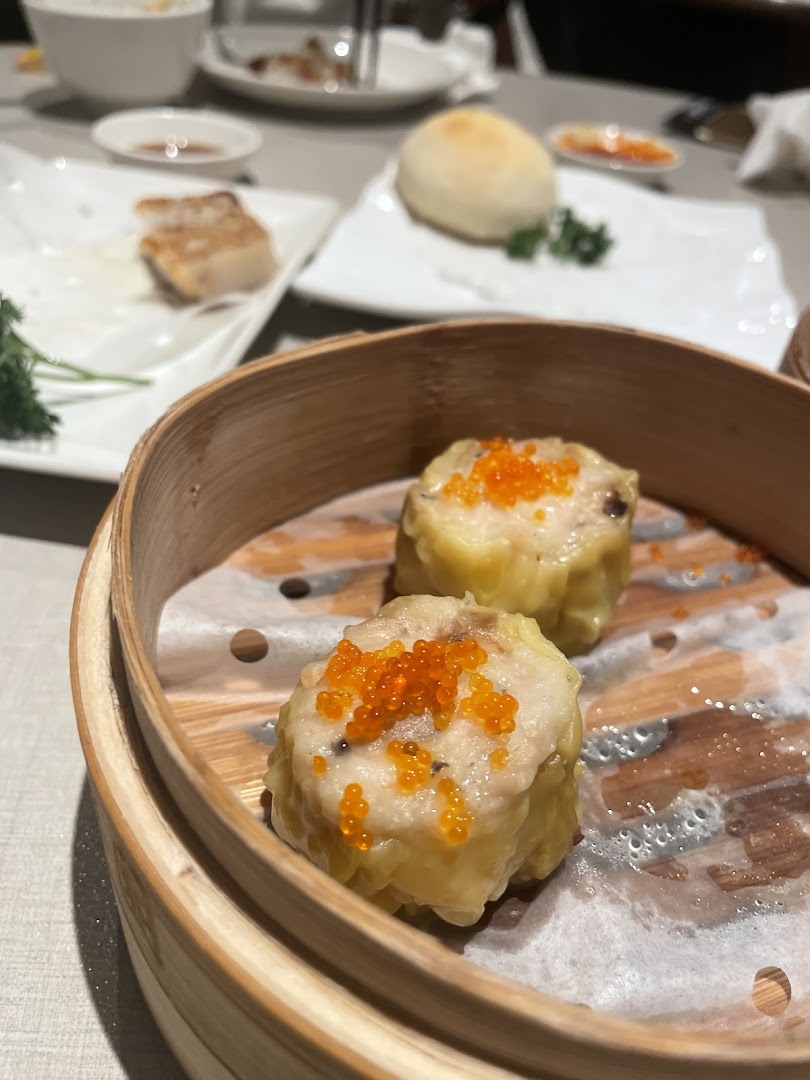 Two siew mai with roe in a bamboo steamer on a restaurant table.