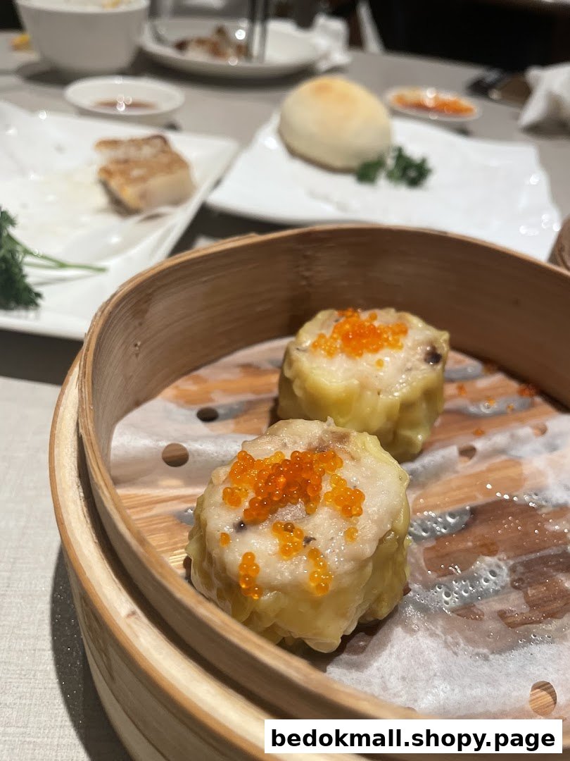 Two siew mai with roe in a bamboo steamer on a restaurant table.